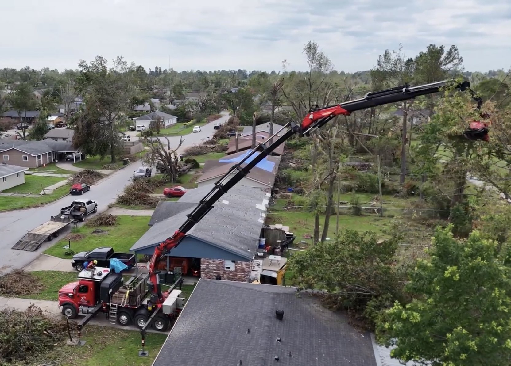 Aerial view of a red crane truck working among storm-damaged homes and trees