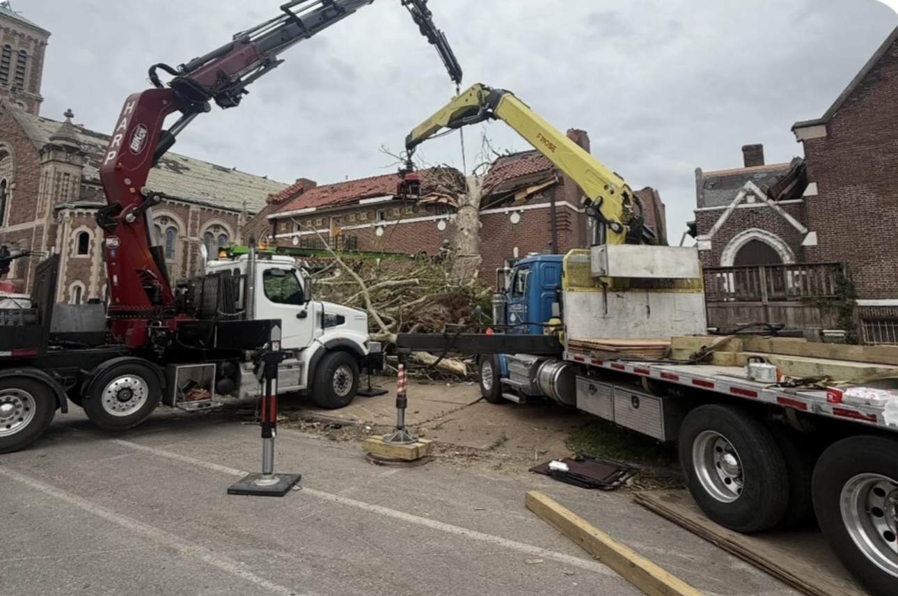 Two crane trucks working a storm-damaged brick building complex