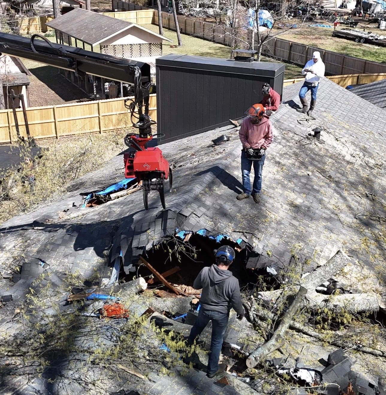 Crew members on a storm-damaged roof beside a crane grapple at the roof opening