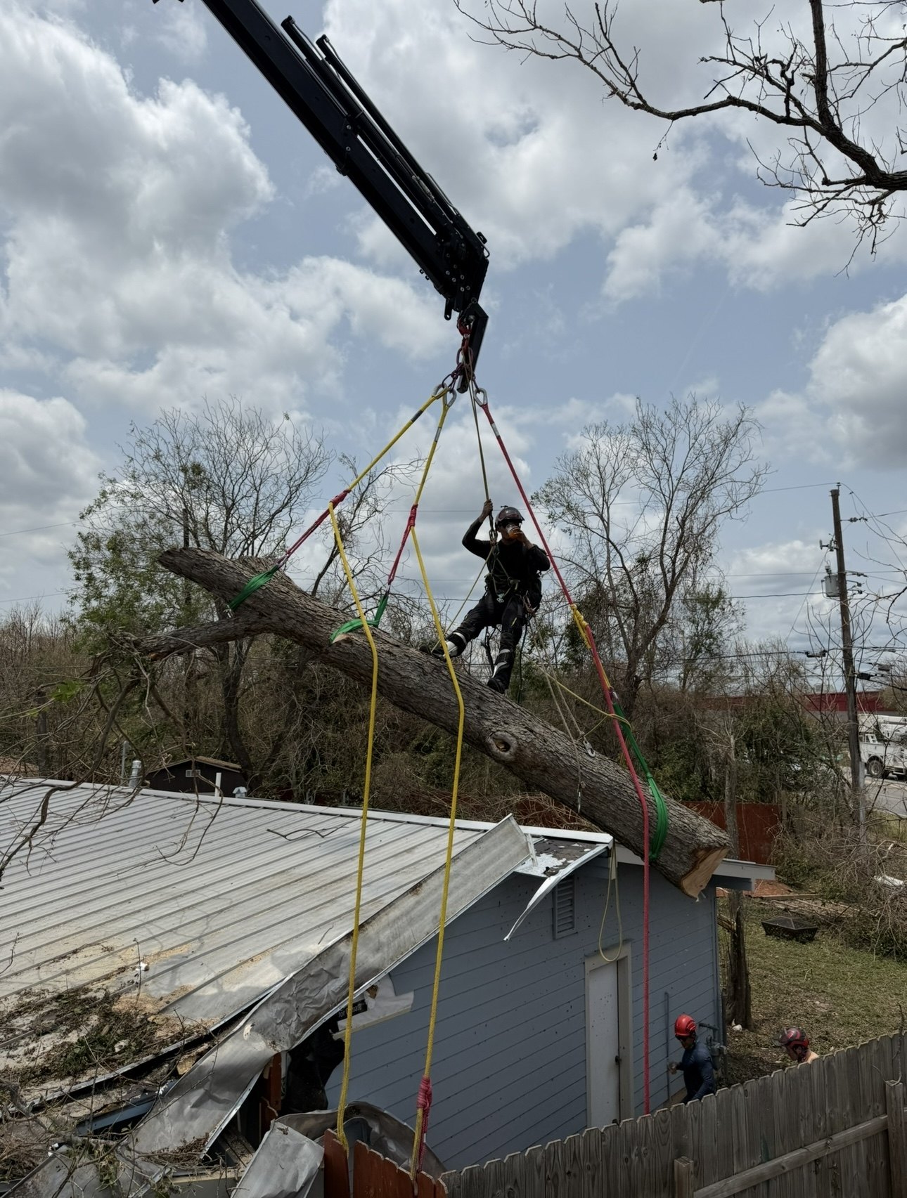 Climber riding a rigged trunk as a crane lifts it off a crushed metal roof