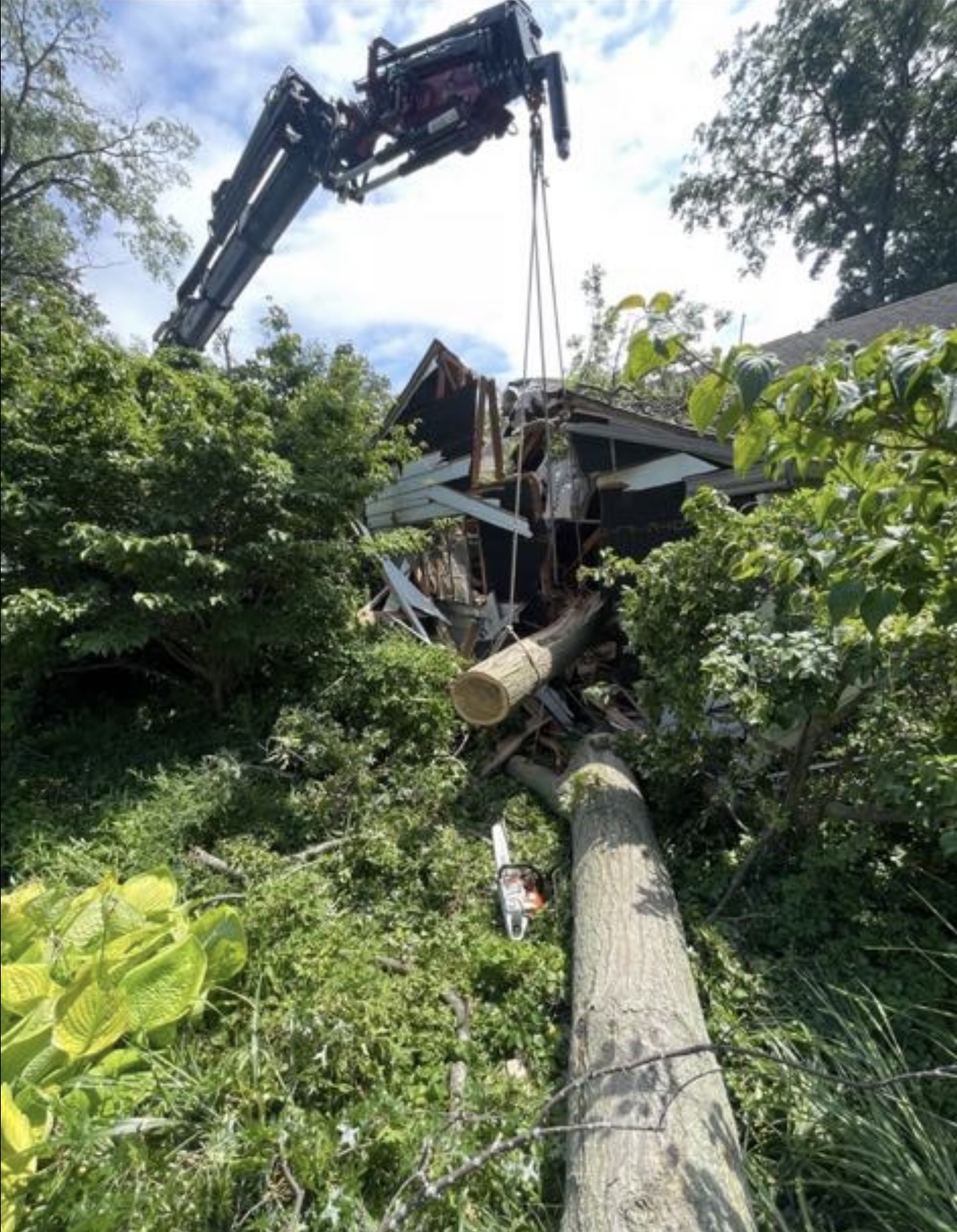 Crane lifting a cut trunk section from a storm-destroyed house